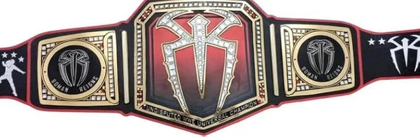 A replica of the WWE Championship belt, featuring a large central gold and red plate with a diamond-embellished cross symbol, flanked by two gold and black side plates with WWE branding.