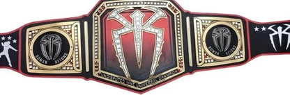 A replica of the WWE Championship belt, featuring a large central gold and red plate with a diamond-embellished cross symbol, flanked by two gold and black side plates with WWE branding.