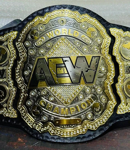 An AEW World Champion belt with a large central plate featuring the AEW logo, surrounded by ornate gold and black detailing, photographed close-up on a dark surface.