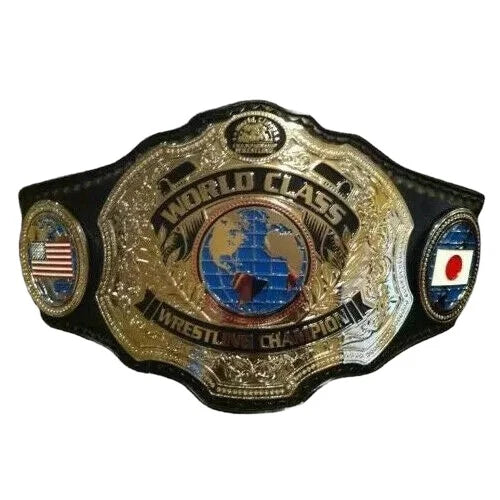 A championship wrestling belt with a large ornate gold-toned central plate reading 'WORLD CLASS WRESTLING CHAMPION,' black side panels, and small circular emblems including an American flag and a Japanese flag, shown on a plain white background.