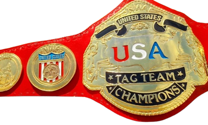 A close-up of a red and gold championship belt with a large central plate reading 'USA TAG TEAM CHAMPIONS' and two smaller gold medallion plates on either side, shown on a white background.