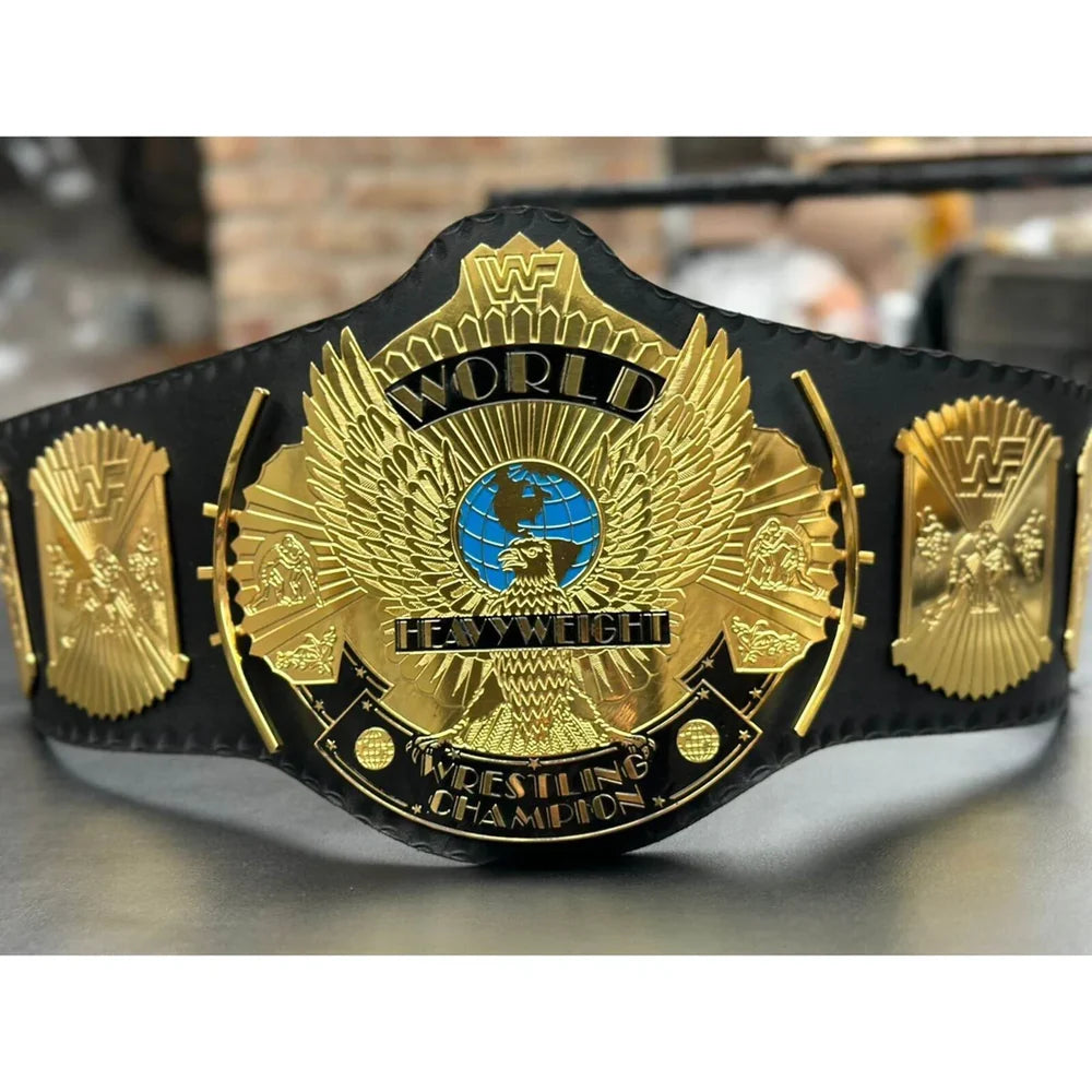 Black and gold wrestling championship belt with detailed emblem on a reflective surface.