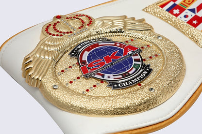 A close-up of a white and gold ISKA World Champion belt, featuring a textured gold central plate with a globe emblem and a red ISKA logo, set against a white padded background.