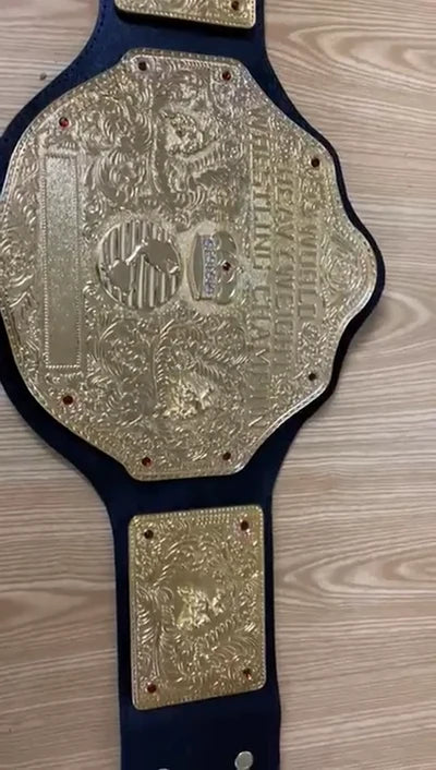 A gold and silver championship belt with an ornate central plate and two smaller matching plates, laid flat on a light wood surface.