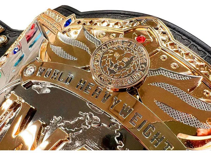 Close-up of a highly detailed championship belt buckle with gold-toned metal plates, engraved text reading 'WORLD HEAVYWEIGHT', a central circular emblem, and small colored gem accents on a black strap.