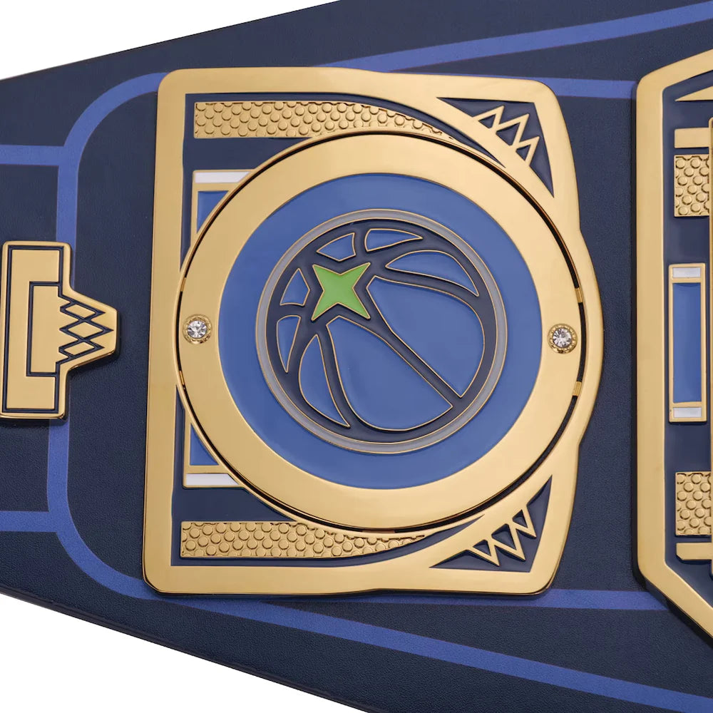 A close-up of a championship-style belt plate with a gold-tone circular frame, blue background, a basketball graphic, and a green star logo. The belt has a dark navy base with blue and gold detailing.