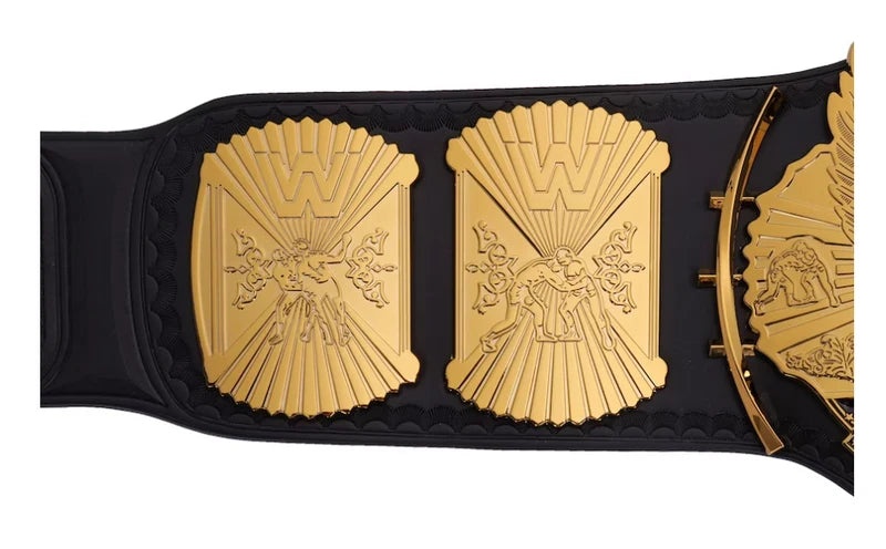 A close-up of a black and gold championship belt with ornate gold plates featuring a raised 'W' logo and sculpted details, shown against a plain white background.