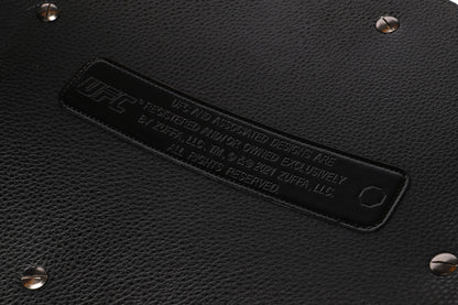 Close-up of a black leather product with a brand label and studs.