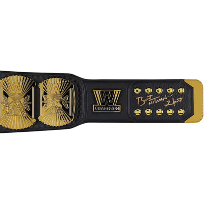 A close-up of a black and gold championship belt strap, featuring two large ornate gold plates, a central 'W CHAMPION' logo, gold studs, and a signature on the right side, set against a plain white background.