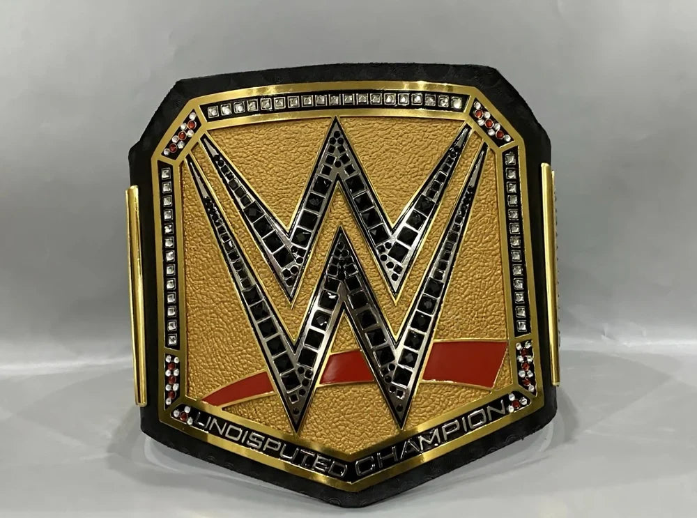 A WWE Undisputed Champion belt featuring a textured gold center with a large black and silver 'W' logo, bordered by rhinestones and red accents, set against a light gray background.