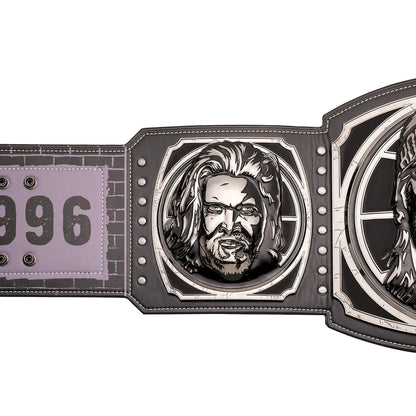 A close-up of a championship-style belt featuring a large engraved metal plate with a portrait, a second engraved plate, and a light purple strap section with the number 096.