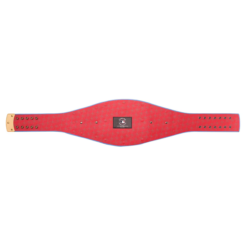 A red leather championship belt with a textured pattern, a central black and red logo patch, and gold-tone metal studs and buckle, shown horizontally on a plain white background.