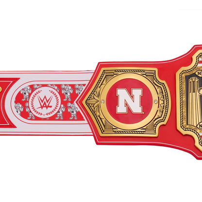 A close-up of a WWE championship belt featuring a red strap and gold-toned metal plates, with a large white letter N in the center and WWE branding visible on the left section.
