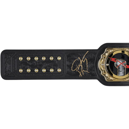 A black leather championship belt with gold hardware, featuring a gold signature in the center and a circular medallion on the right, shown against a plain white background.