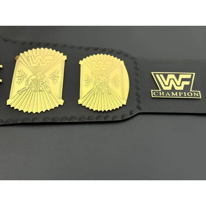 A black leather championship belt featuring two large gold-plated winged 'W' plates and a gold 'WF CHAMPION' logo plate on the strap, displayed on a dark gray background.