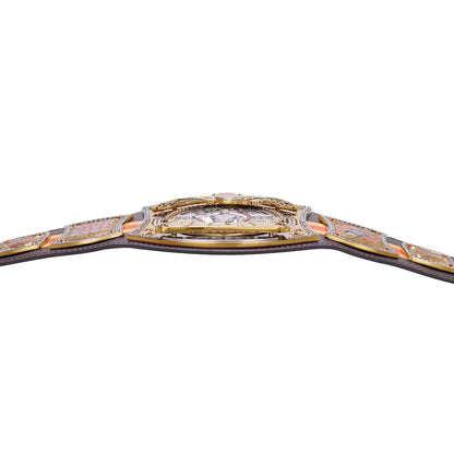 A close-up of a championship-style belt across a white background, showing ornate gold-toned metal plates, a central buckle area with a clear stone, and a dark strap extending off both sides.