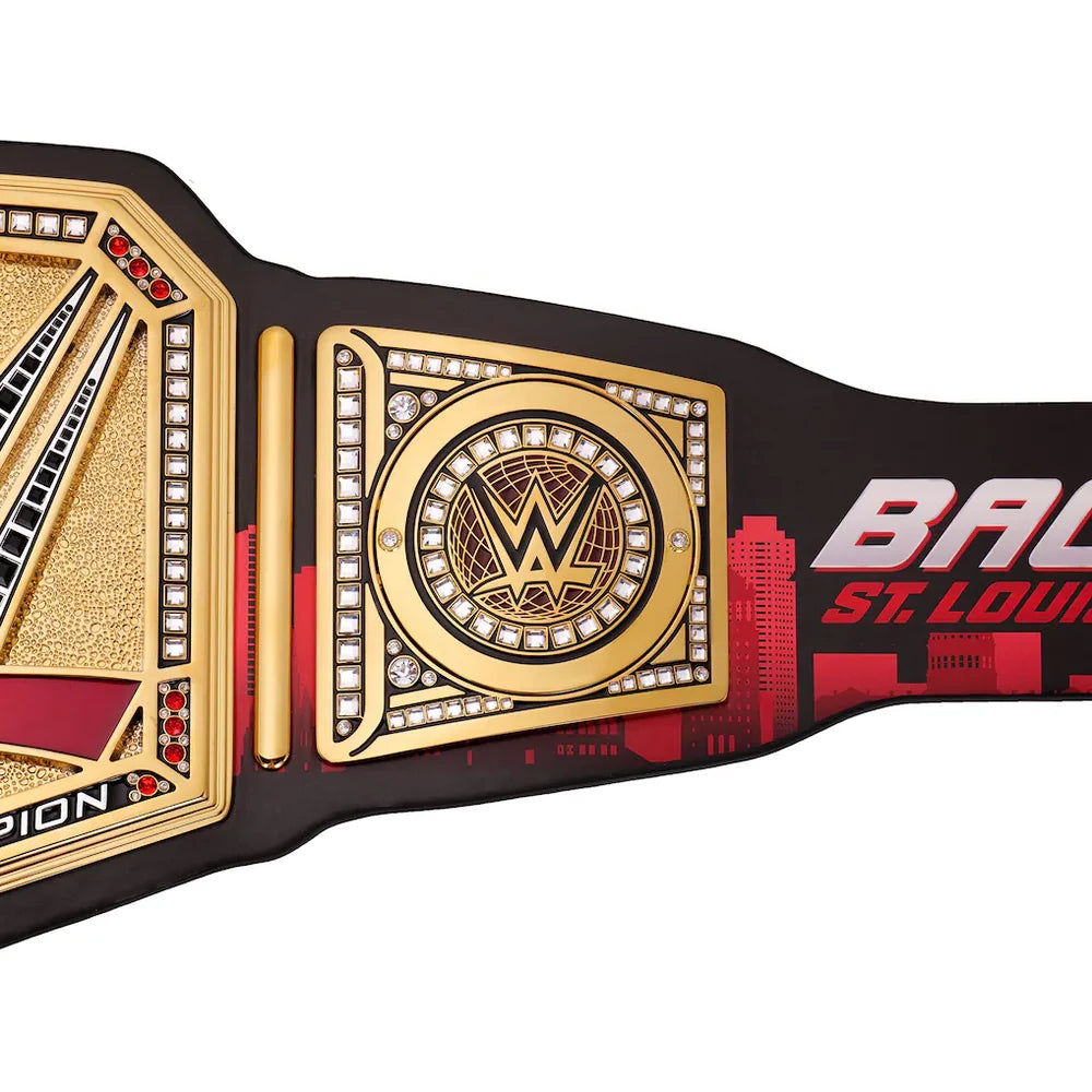 A close-up of a WWE Championship belt featuring gold-plated plates, clear rhinestones, and a black strap printed with red and white graphics and the text 'BATTLE ST. LOUIS'.