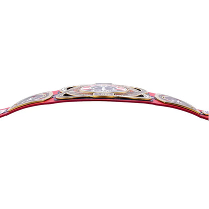 A close-up of a red championship belt with ornate silver and gold metal plates, shown against a plain white background.