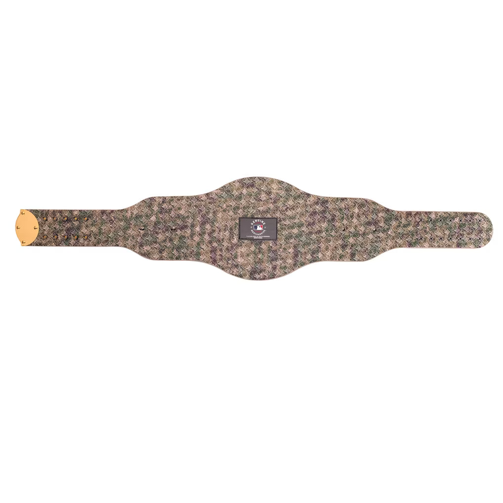 A camouflage-patterned belt with a central black label and a small gold-toned circular emblem on the left end, shown against a plain white background.