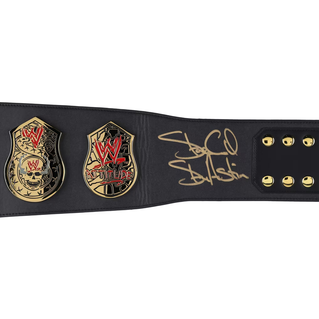 A black leather WWE Championship belt featuring two gold-tone championship plates with red and black detailing, and a gold signature on the strap, shown against a plain white background.