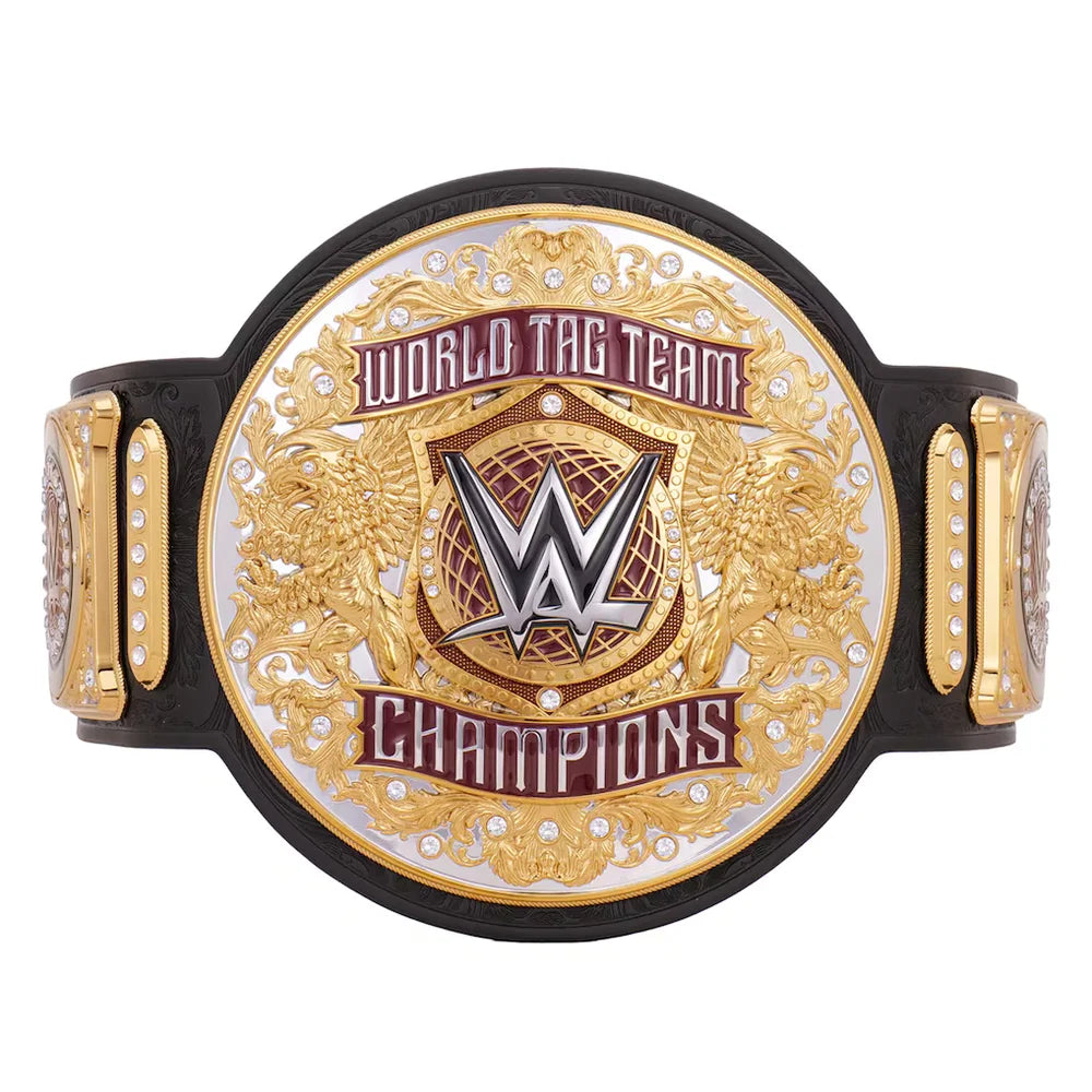 A WWE World Tag Team Champions belt featuring a large oval gold and silver plate with the WWE logo in the center, flanked by two smaller gold plates with rhinestone accents, all mounted on a black strap against a white background.