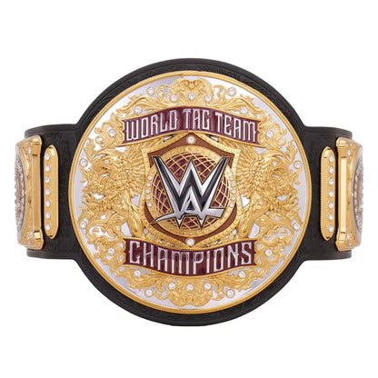 A WWE World Tag Team Champions belt featuring a large oval gold and silver plate with the WWE logo in the center, flanked by two smaller gold plates with rhinestone accents, all mounted on a black strap against a white background.