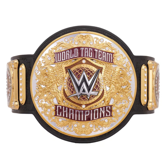 A WWE World Tag Team Champions belt featuring a large oval gold and silver plate with the WWE logo in the center, flanked by two smaller gold plates with rhinestone accents, all mounted on a black strap against a white background.