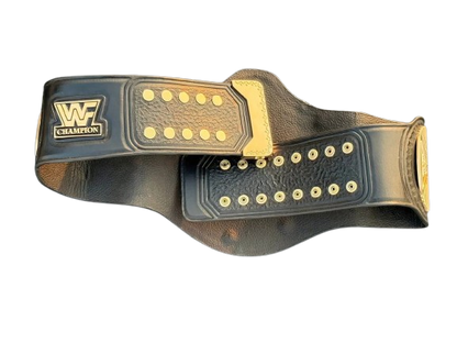 A black leather championship belt with gold-toned metal studs, a gold buckle, and a gold 'WF CHAMPION' logo patch on the left side, shown against a plain white background.
