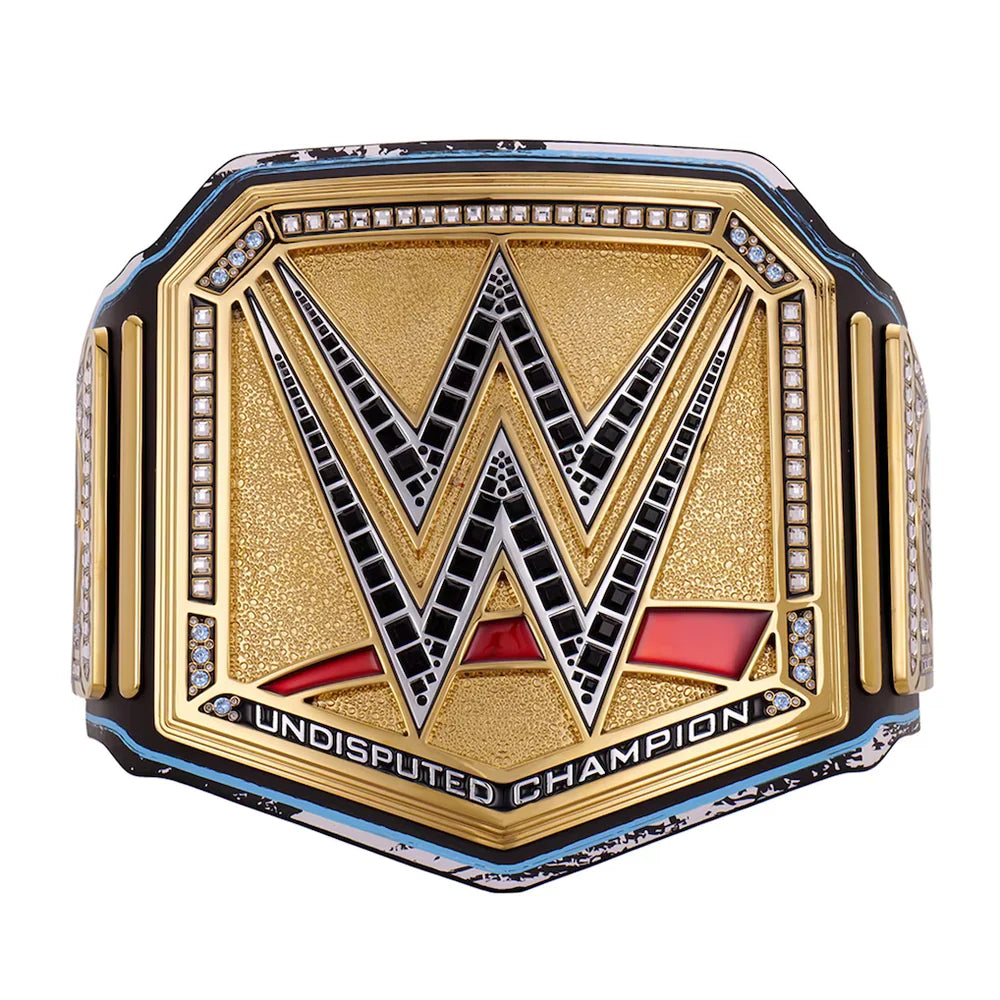 WWE Undisputed Champion belt featuring a gold-toned central plate with a large black and silver WWE logo, bordered by small clear stones, with red and black lower detailing and the words 'UNDISPUTED CHAMPION' on a white background.