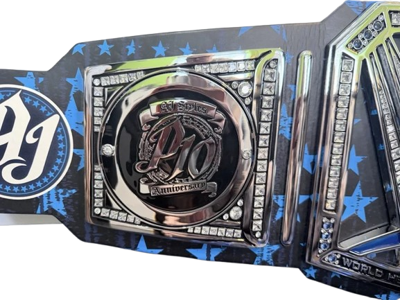 A close-up of a championship belt featuring a central round plate with the letters 'PJ' and 'anniversary 2025,' surrounded by rhinestone borders, on a black and blue star-patterned strap.