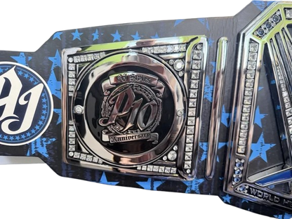A close-up of a championship belt featuring a central round plate with the letters 'PJ' and 'anniversary 2025,' surrounded by rhinestone borders, on a black and blue star-patterned strap.