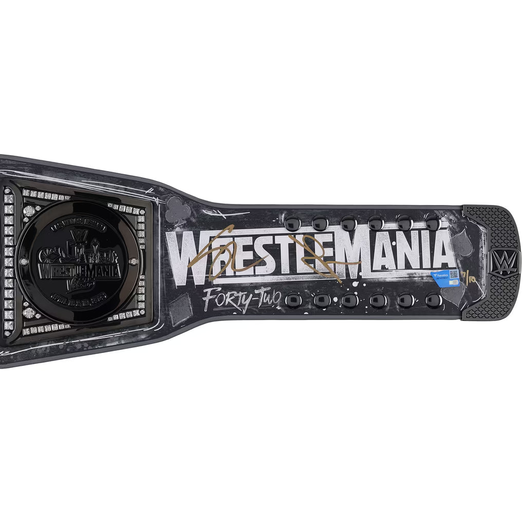 A signed WrestleMania Forty-Two championship belt from WWE, featuring a black and gray textured design with gold signatures and white lettering, set against a plain white background.