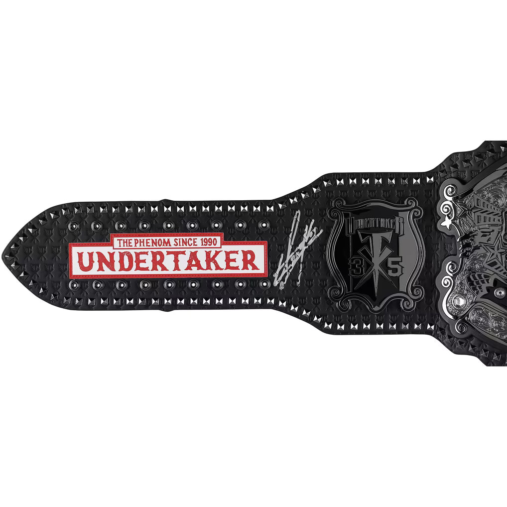 A close-up of a black leather wrestling championship belt, specifically the Undertaker belt, featuring a red and white 'UNDERTAKER' nameplate, silver studded edges, and an embossed black crest with silver details.