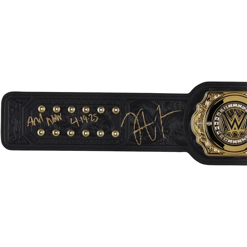 A WWE championship belt featuring a black leather strap with gold hardware, a large WWE logo medallion on the right, and gold signatures and date engravings on the left.