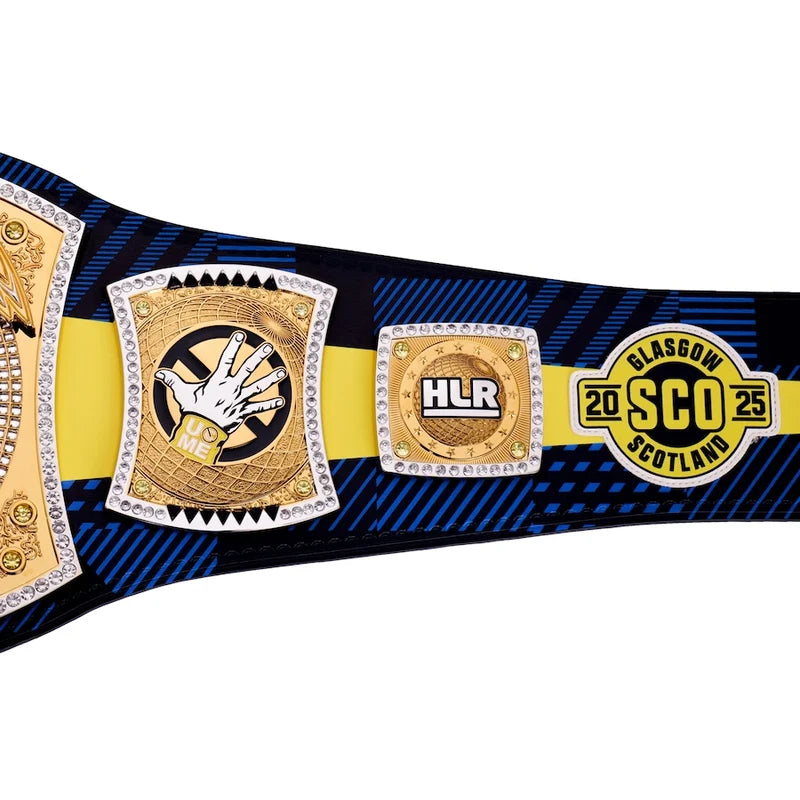 A close-up of a championship belt with gold and silver plates, a yellow center stripe, and a blue patterned strap. The right plate reads 'GLASGOW SCOTLAND 2025'.