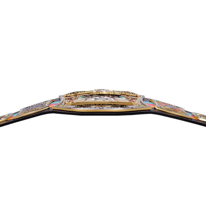 A close-up of a championship belt across a white background, showing gold-toned metal plates, colorful gemstone accents, and a black strap.